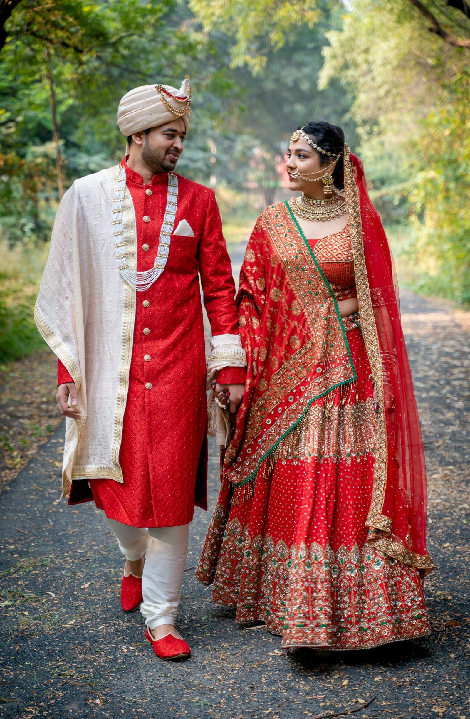 A couple in traditional wedding attire holding hands and walking on a path